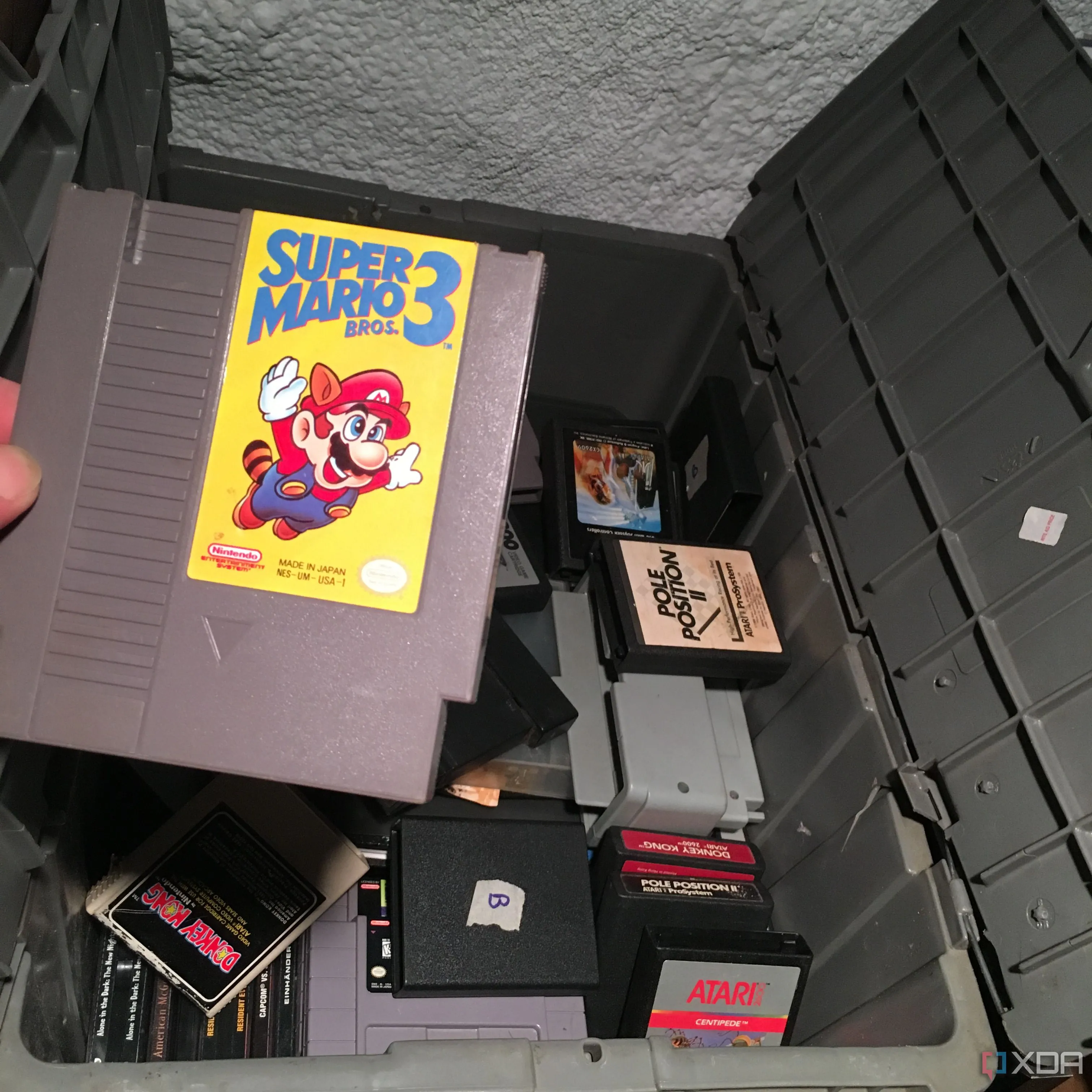 Game thủ cầm băng Super Mario Bros 3 của NES lên từ một chiếc hộp chứa đầy game retro cũ