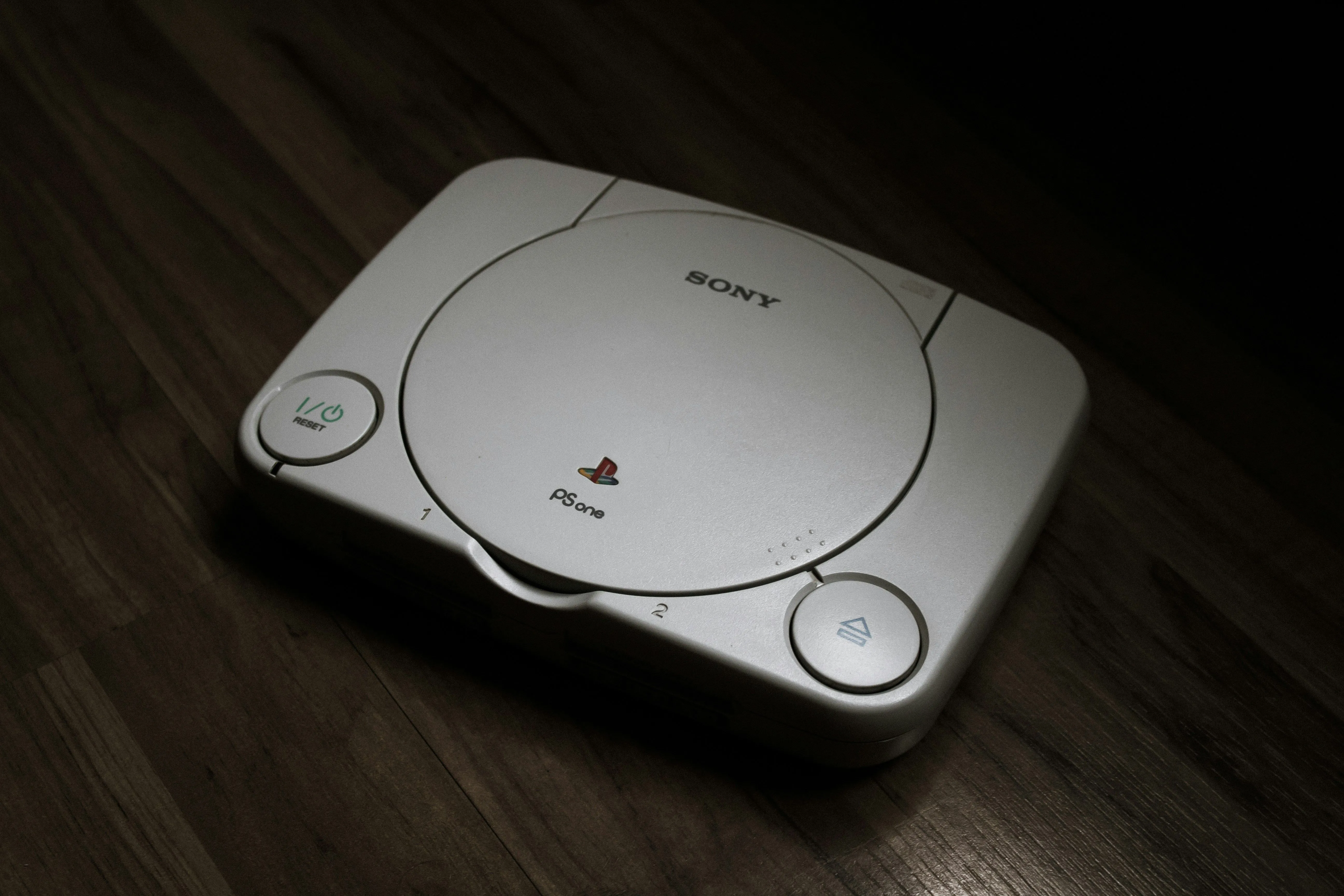 Máy chơi game console PlayStation 1 màu xám đặt trên sàn gỗ