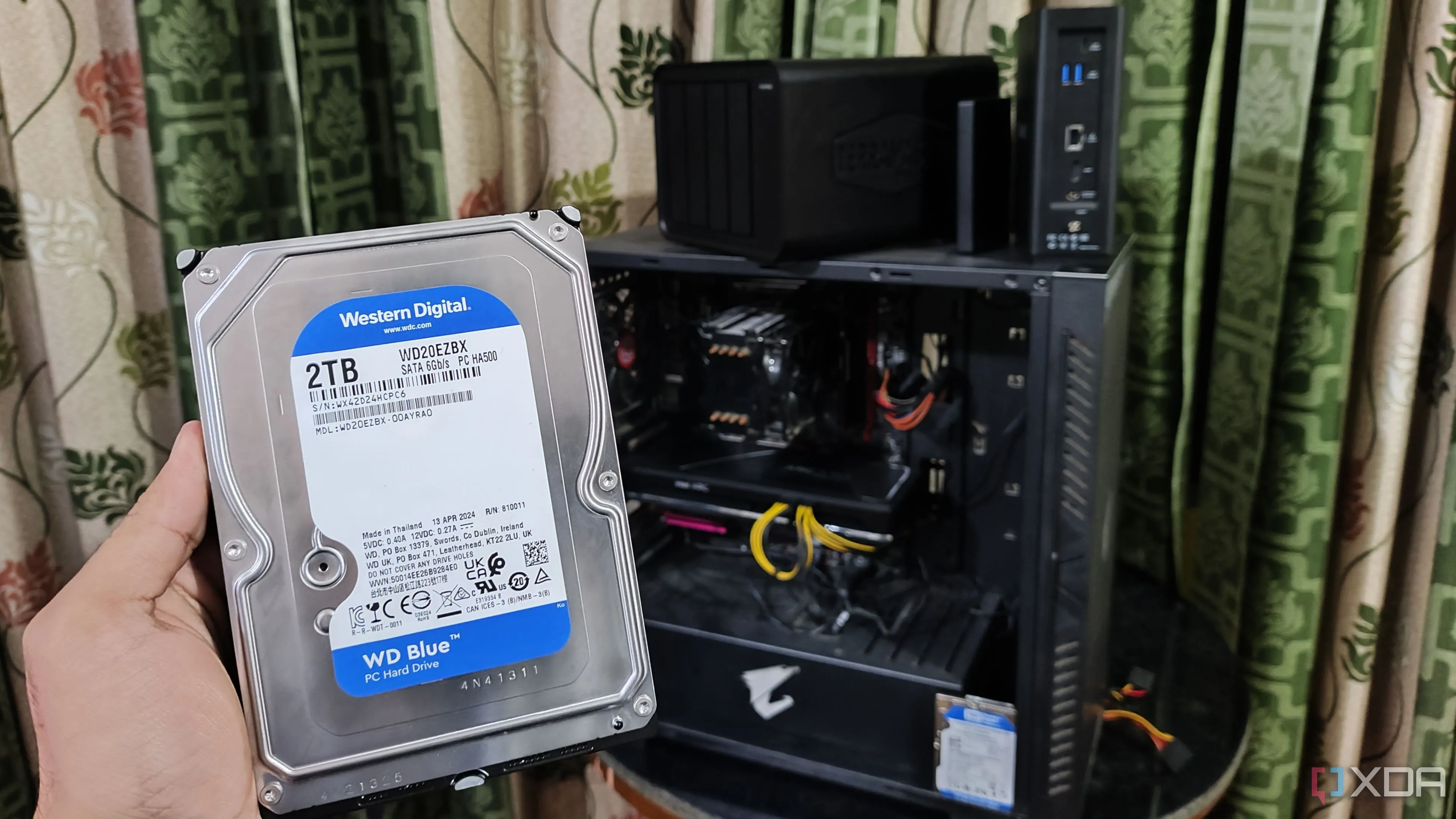 Một người đang cầm ổ cứng HDD trước máy tính và hai thiết bị NAS TerraMaster, nhấn mạnh nhu cầu lưu trữ tăng cao