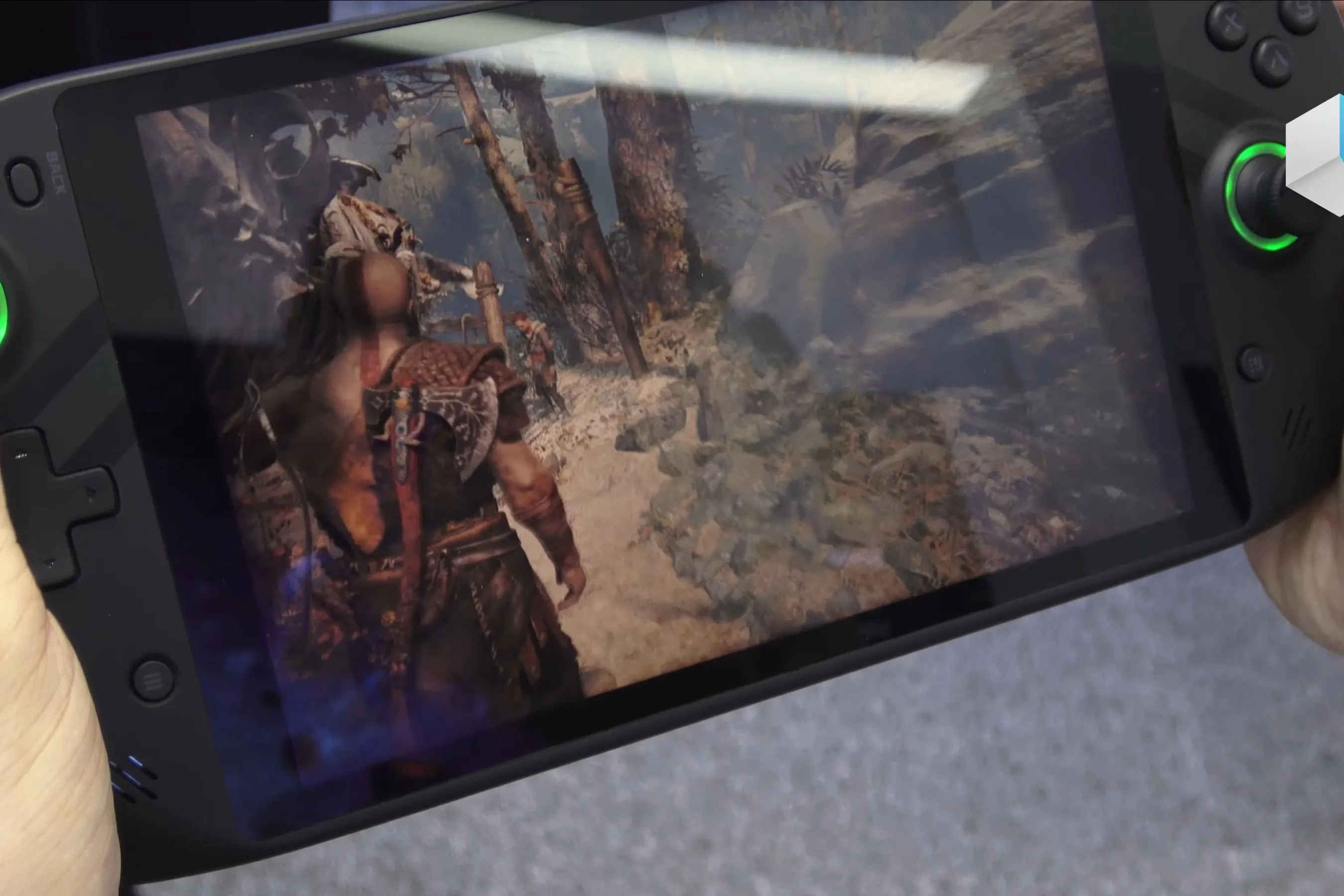 Một thiết bị PC chơi game cầm tay đang chạy game God of War, hiển thị cảnh Kratos và Atreus