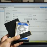 Người đang cầm SSD, HDD nội bộ và HDD gắn ngoài trước màn hình hiển thị giao diện Proxmox