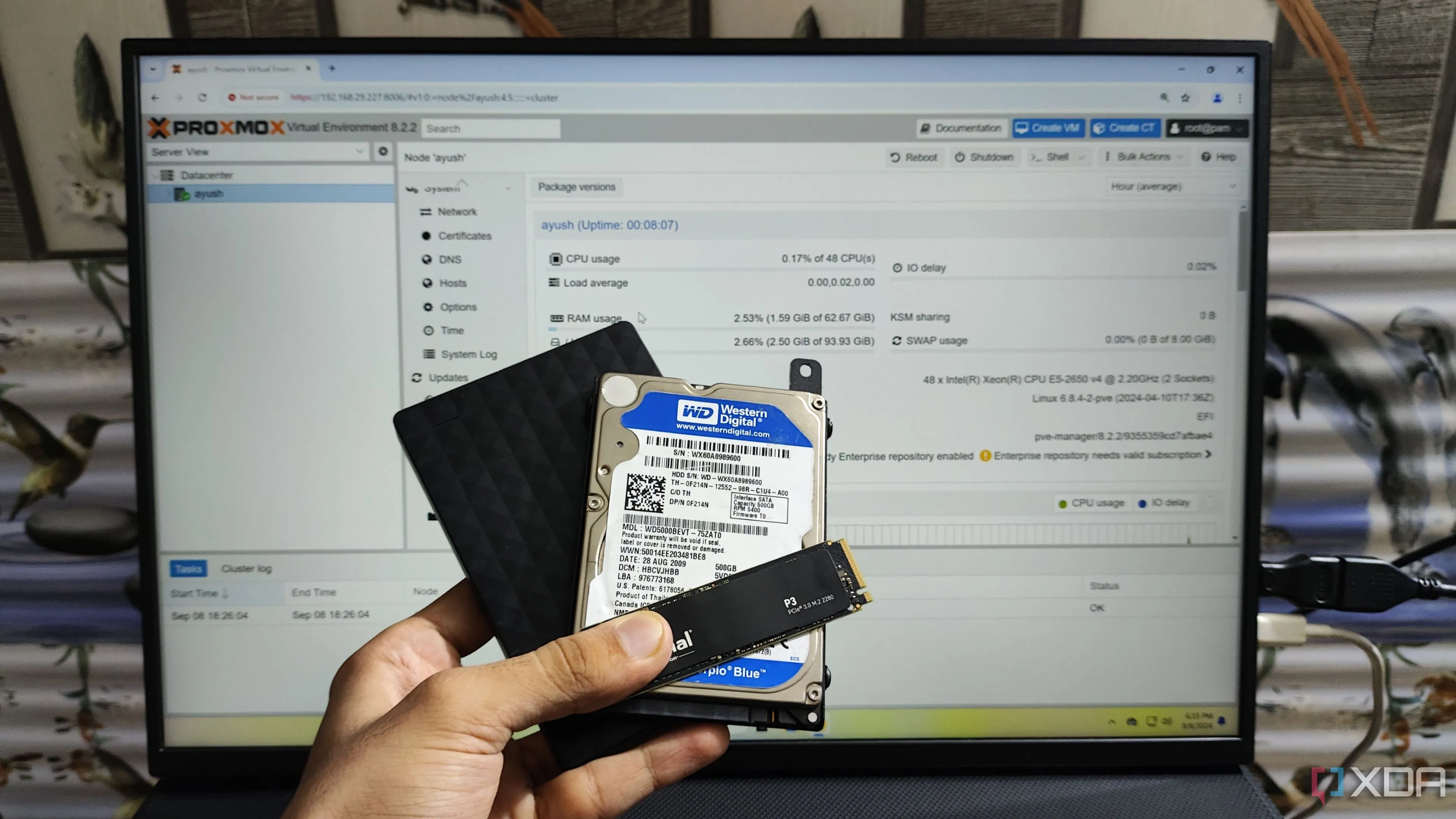 Người đang cầm SSD, HDD nội bộ và HDD gắn ngoài trước màn hình hiển thị giao diện Proxmox