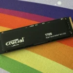 Ổ cứng SSD Crucial T705 NVMe PCIe Gen5 trên bàn làm việc có thảm lót màu cầu vồng, thể hiện tốc độ và hiệu suất cao của thiết bị