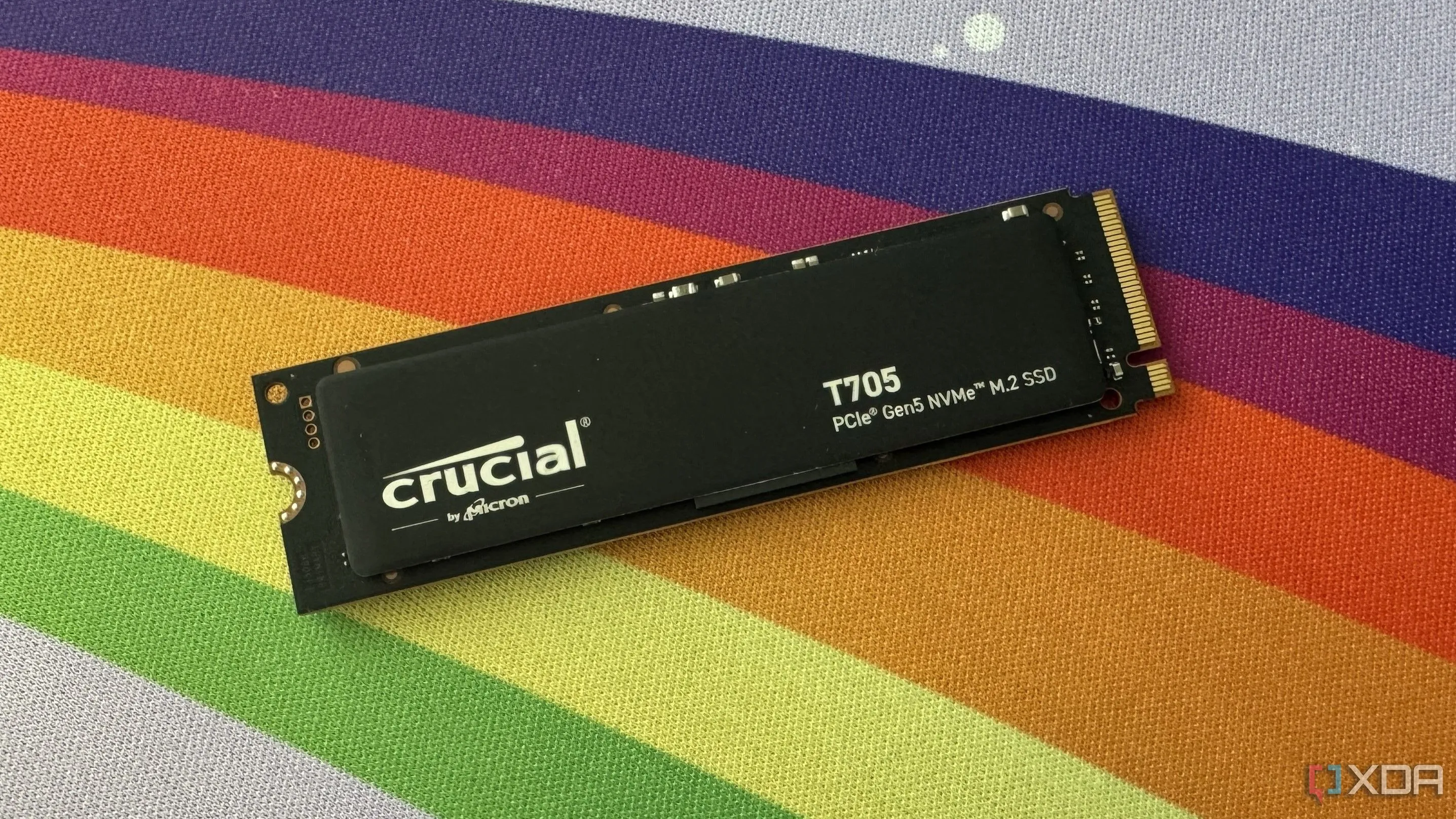 Ổ cứng SSD Crucial T705 NVMe PCIe Gen5 trên bàn làm việc có thảm lót màu cầu vồng, thể hiện tốc độ và hiệu suất cao của thiết bị